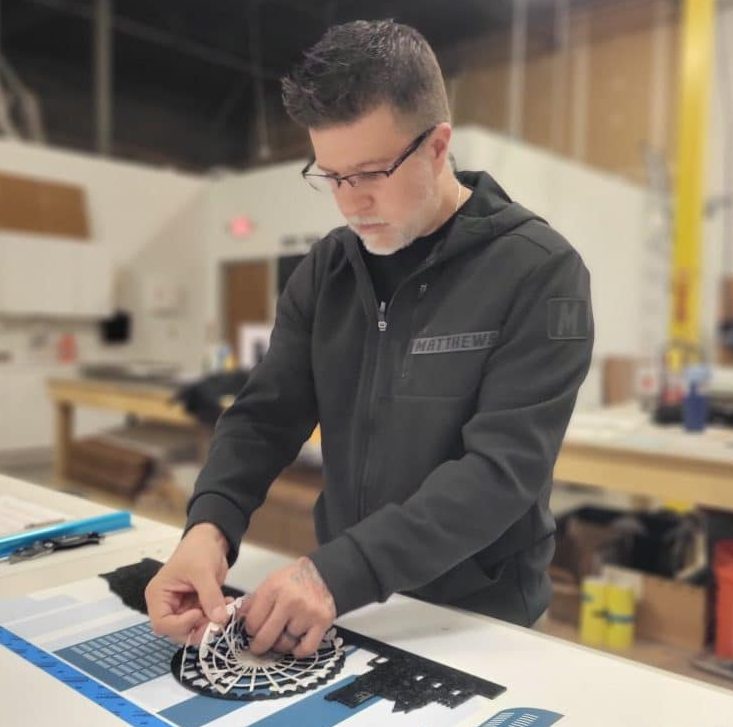 Man working on a custom sign project in a workshop, demonstrating attention to detail and craftsmanship for High Stakes Creative's branding solutions.