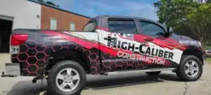 Pickup truck with a bold, colorful wrap advertising High-Caliber Construction.