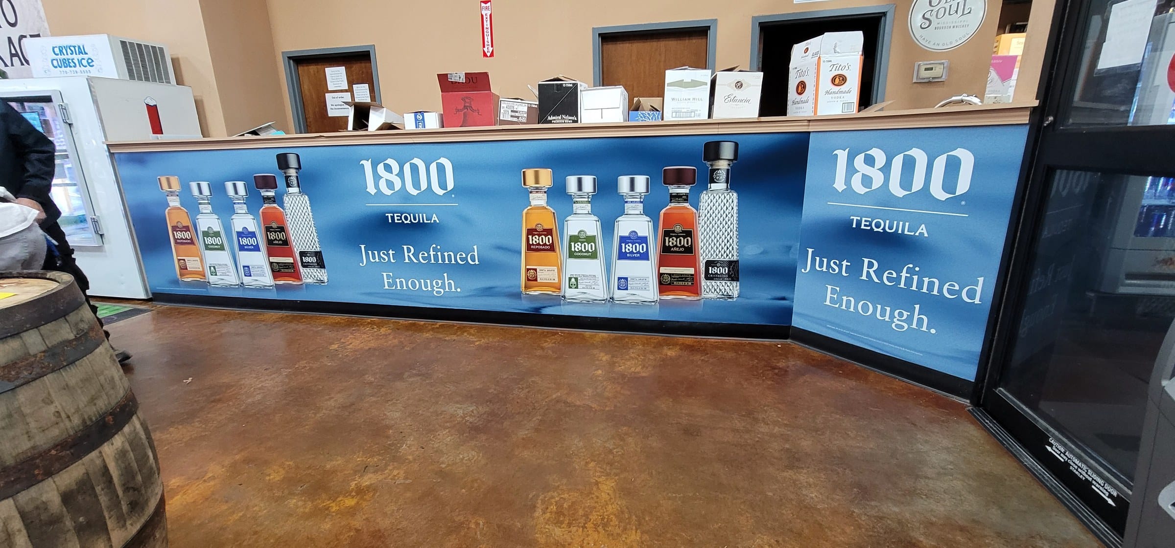 Curved liquor-store checkout counter wrapped in blue 1800 Tequila graphics ("Just Refined , 1800 Tequila, by High Stakes Creative