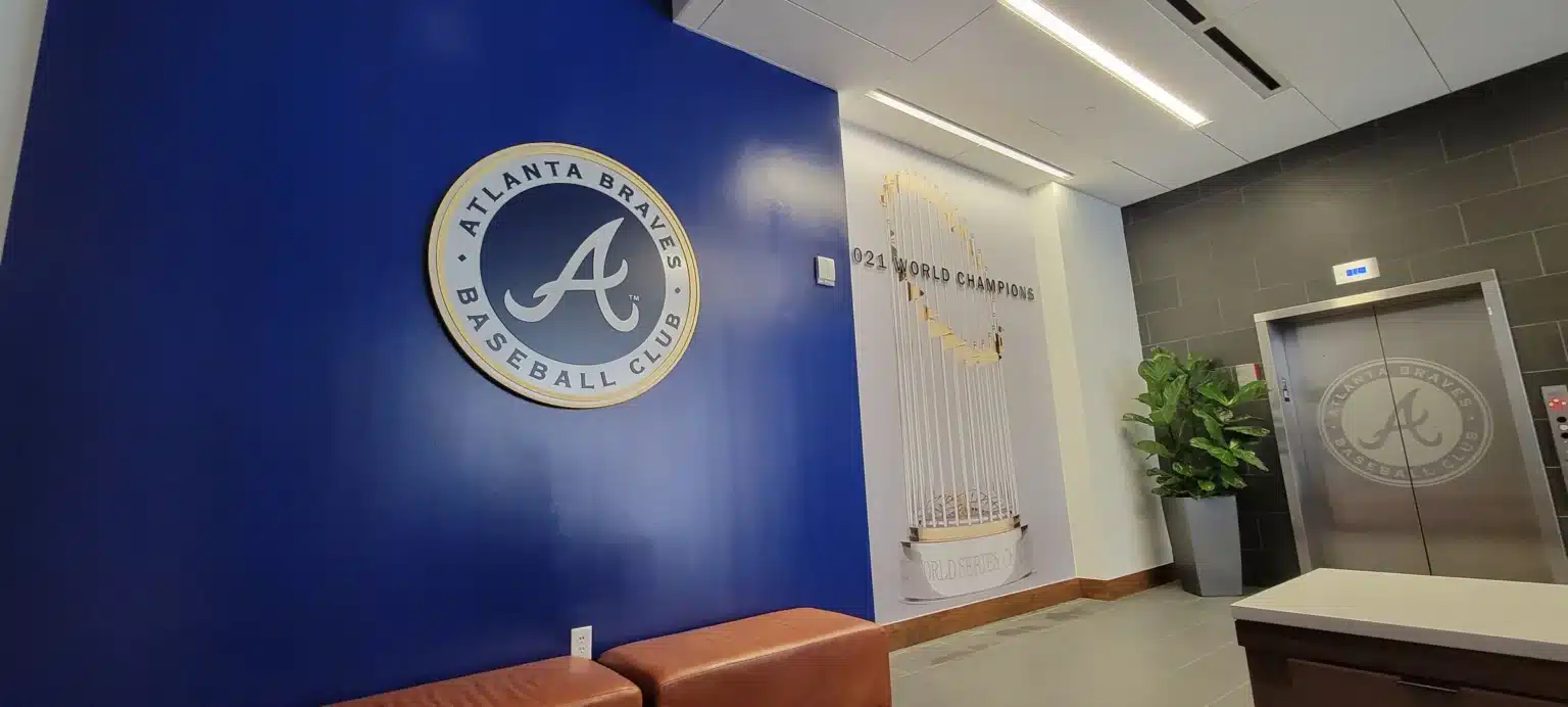 Dimensional Atlanta Braves Baseball Club logo mounted on a navy lobby wall, with the World Champions trophy graphic in the background, by High Stakes Creative