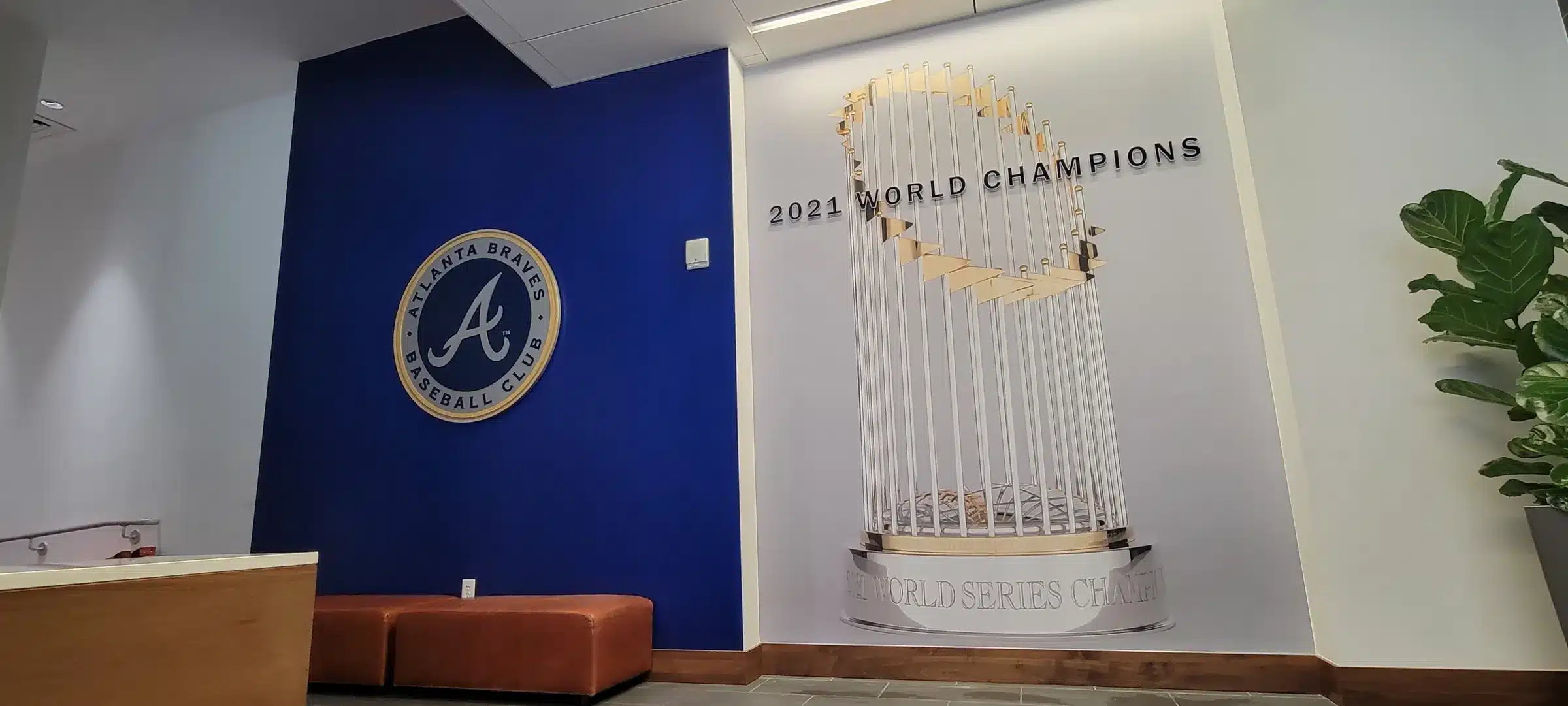 Atlanta Braves lobby with a navy feature wall holding a dimensional Braves logo beside a 2021 World Champions trophy wall graphic, by High Stakes Creative