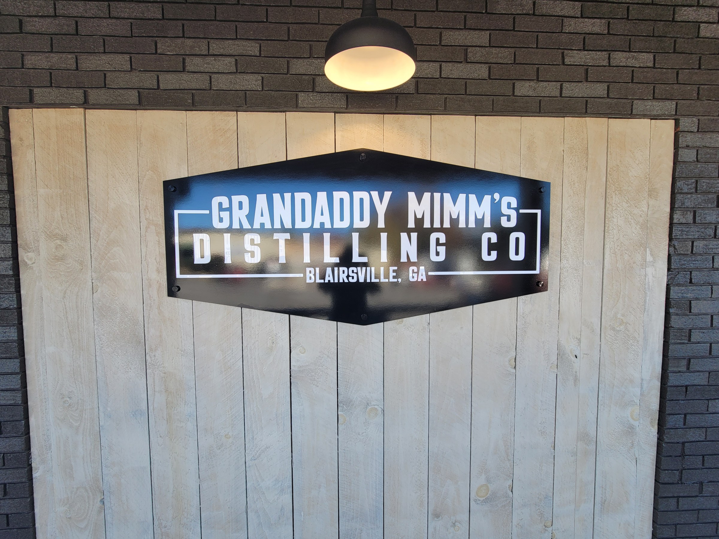 Hexagonal panel sign on whitewashed plank wall under barn light, Grandaddy Mimm's Distilling Co., Blairsville, GA, by High Stakes Creative