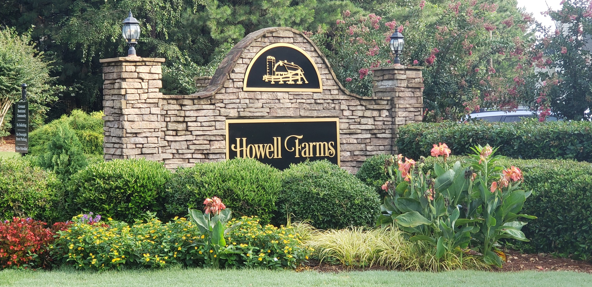 Stacked-stone entrance monument with Howell Farms panel and farm crest, flowers in front, Howell Farms, by High Stakes Creative