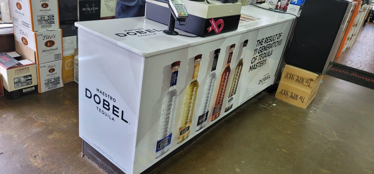 Printed wrap on liquor-store checkout counters showing Maestro Dobel bottles and tagline, Maestro Dobel Tequila, by High Stakes Creative