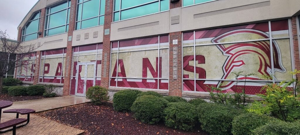 Large SPARTANS lettering and Spartan helmet graphics across school building windows, Spartans, by High Stakes Creative