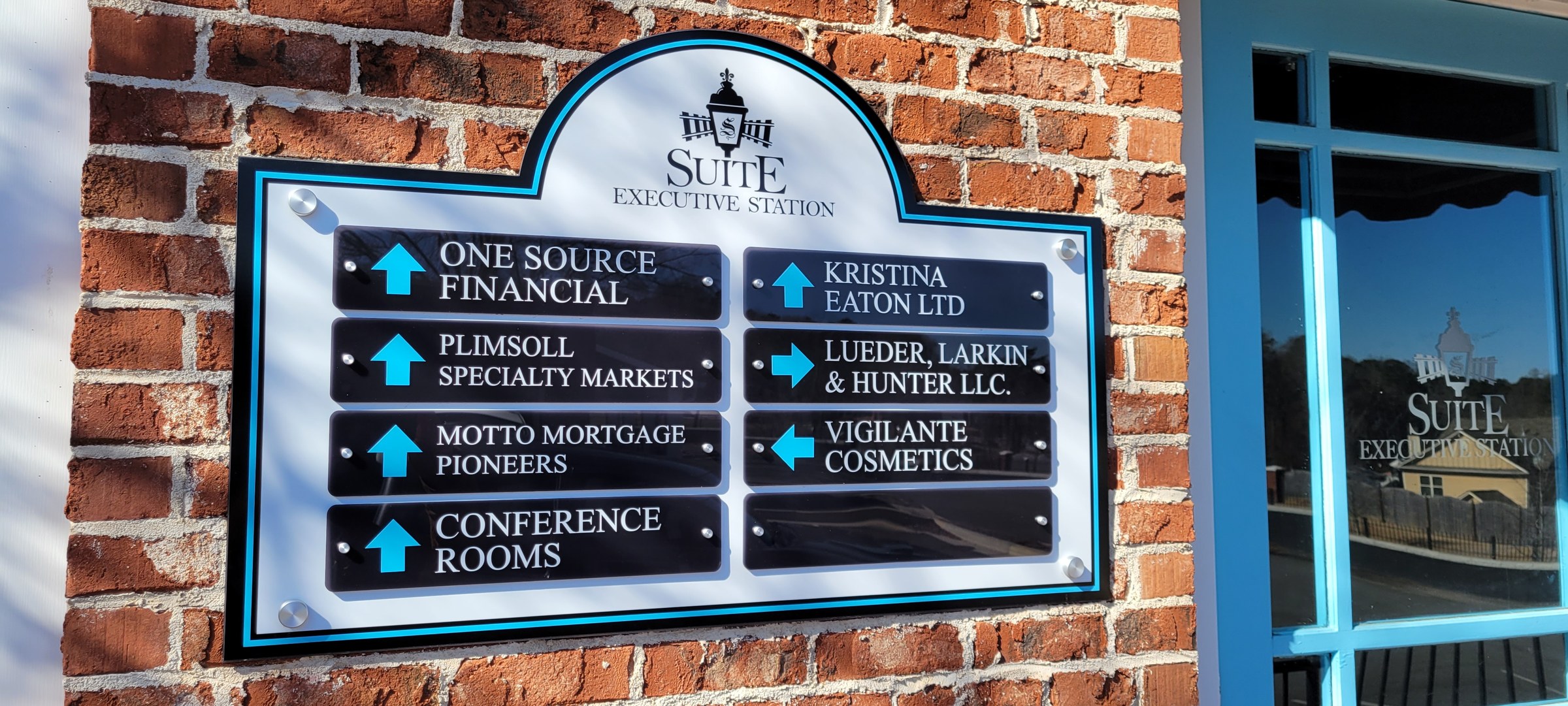 Shaped tenant directory sign with arrow panels mounted on brick next to entry glass with l, Suite Executive Station, by High Stakes Creative