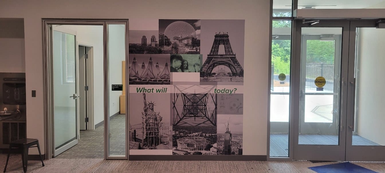 Long black-and-white photo collage corridor mural (landmarks, adventure scenes) with "What, by High Stakes Creative